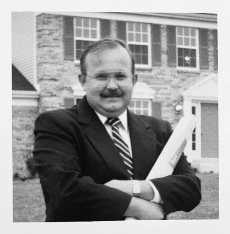 Vintage photograph of a man in a suit standing in front of a stone house, representing the early days of Fischer Homes