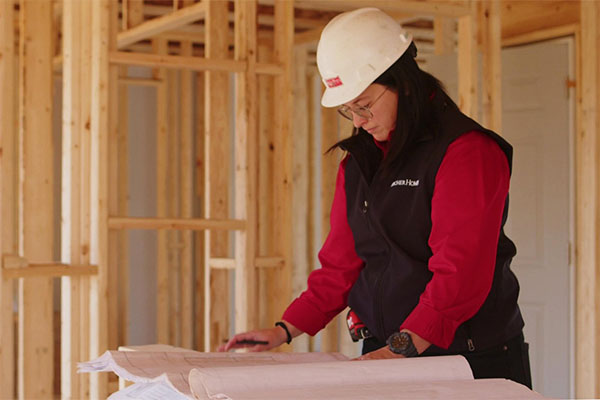 Fischer Homes associate wearing a white hard hat and red vest studies construction plans inside a Fischer Homes house under construction