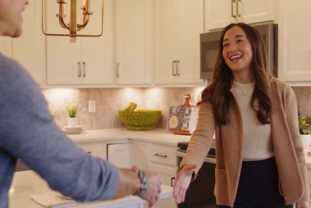 Smiling woman stands in a modern kitchen extending her hand for a handshake during a meeting.